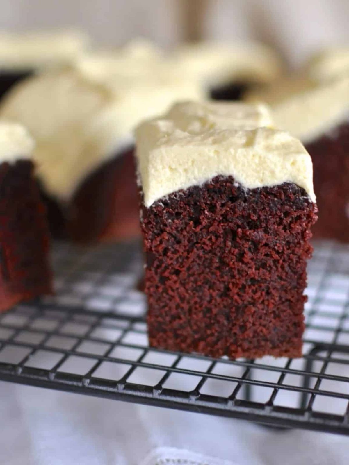 Square of Best Red velvet cake with buttercream icing (frosting) on a wire rack.