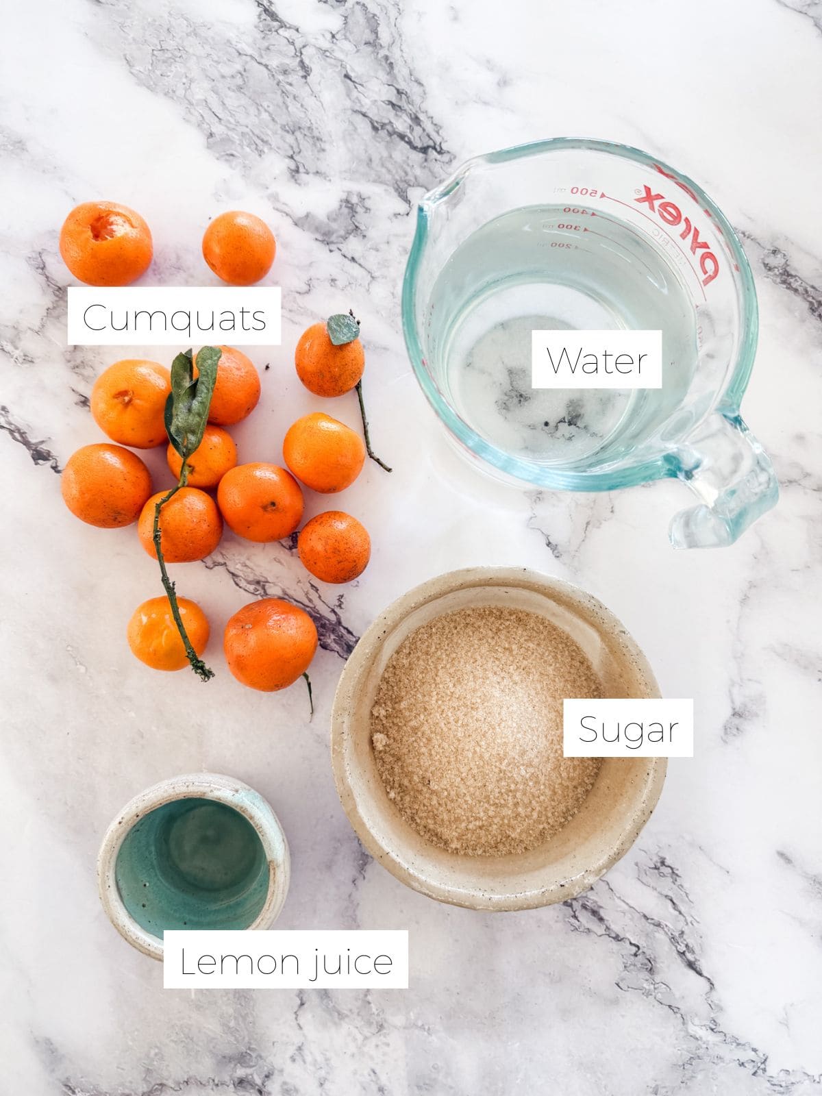 Ingredients for cumquat jam. Cumquats, measuring cup with water, bowl with raw sugar and bowl with lemon juice on marble look bench top.