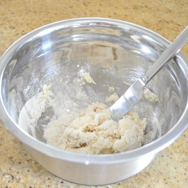 Mixing water cracker dough in a silver bowl using a silver butter knife.