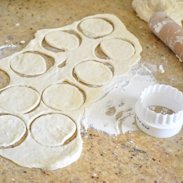 Cutting out rolled water cracker dough on a bench top.