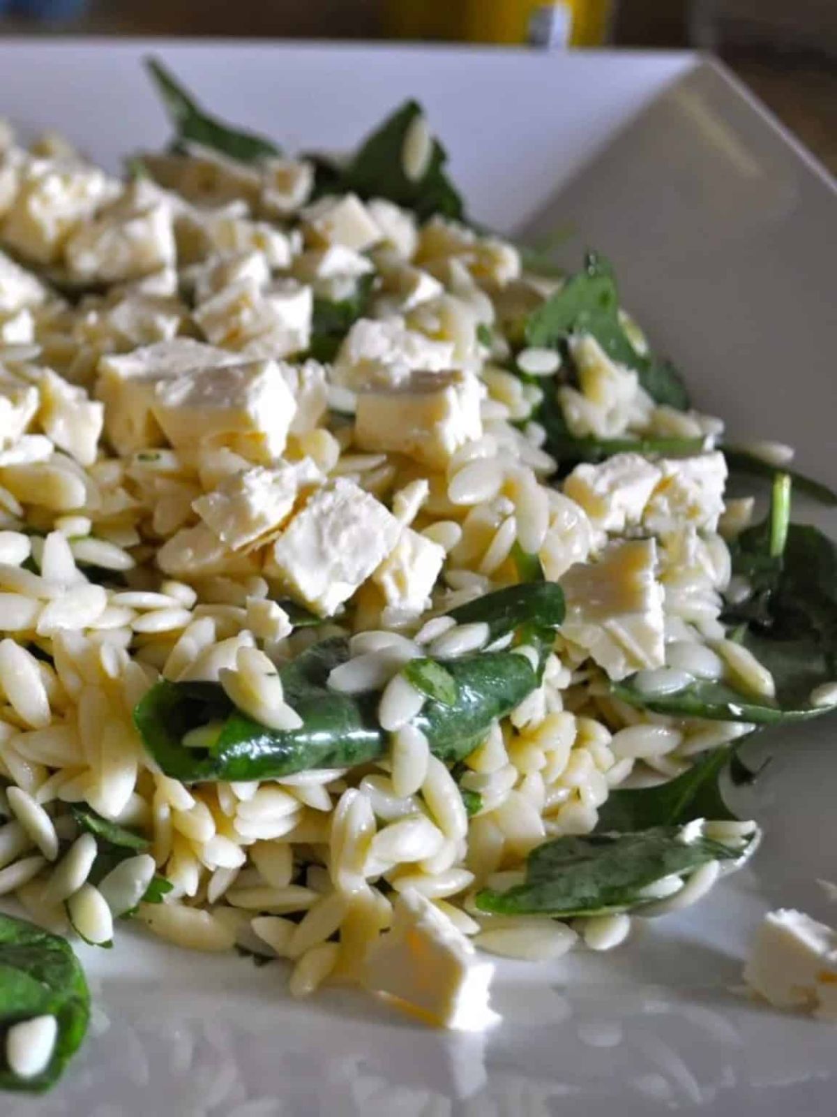Orzo, spinach, beans & feta combined in orzo salad on a white platter.