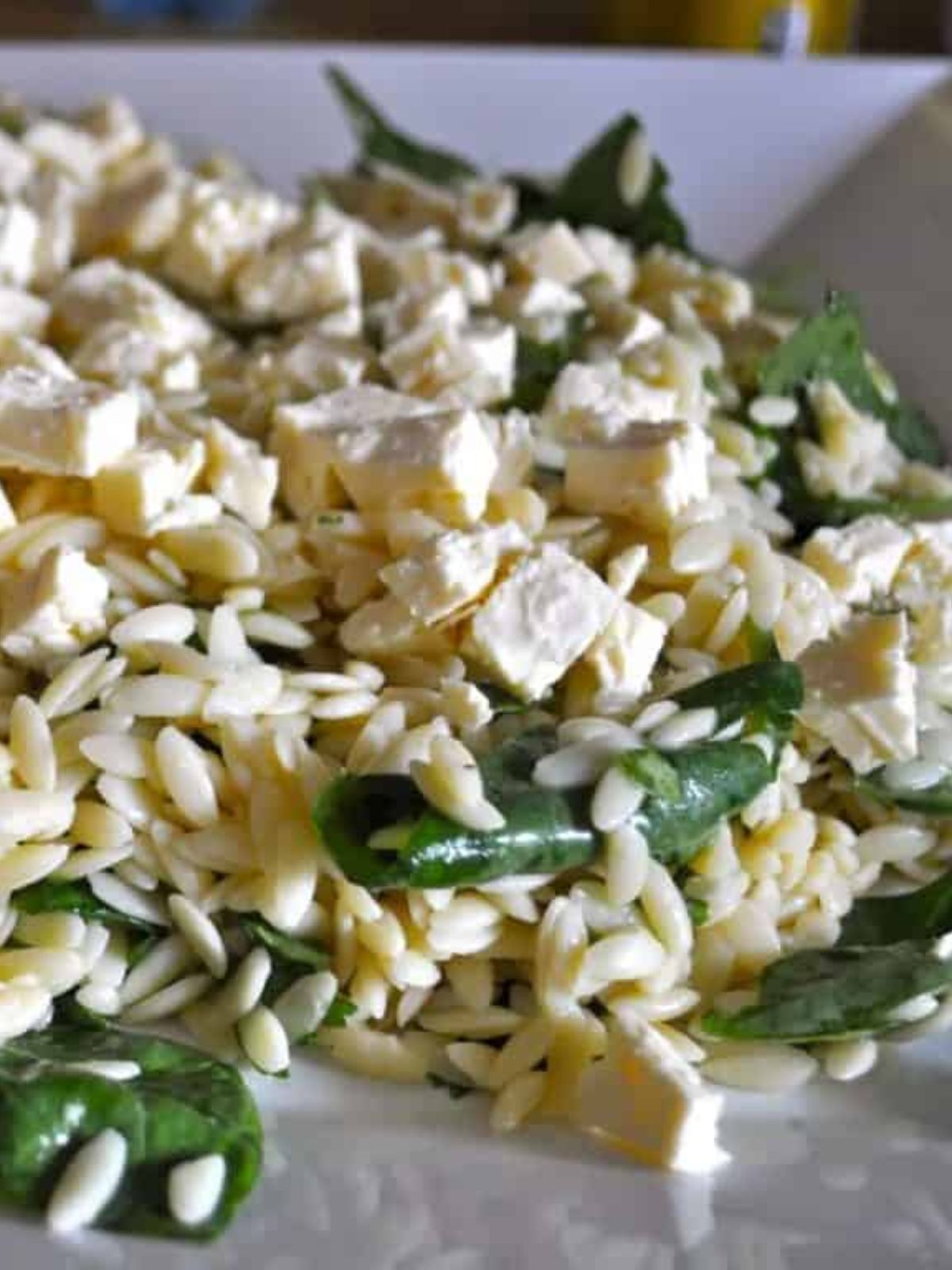 Orzo, spinach, beans & feta combined in orzo salad on a white platter. 