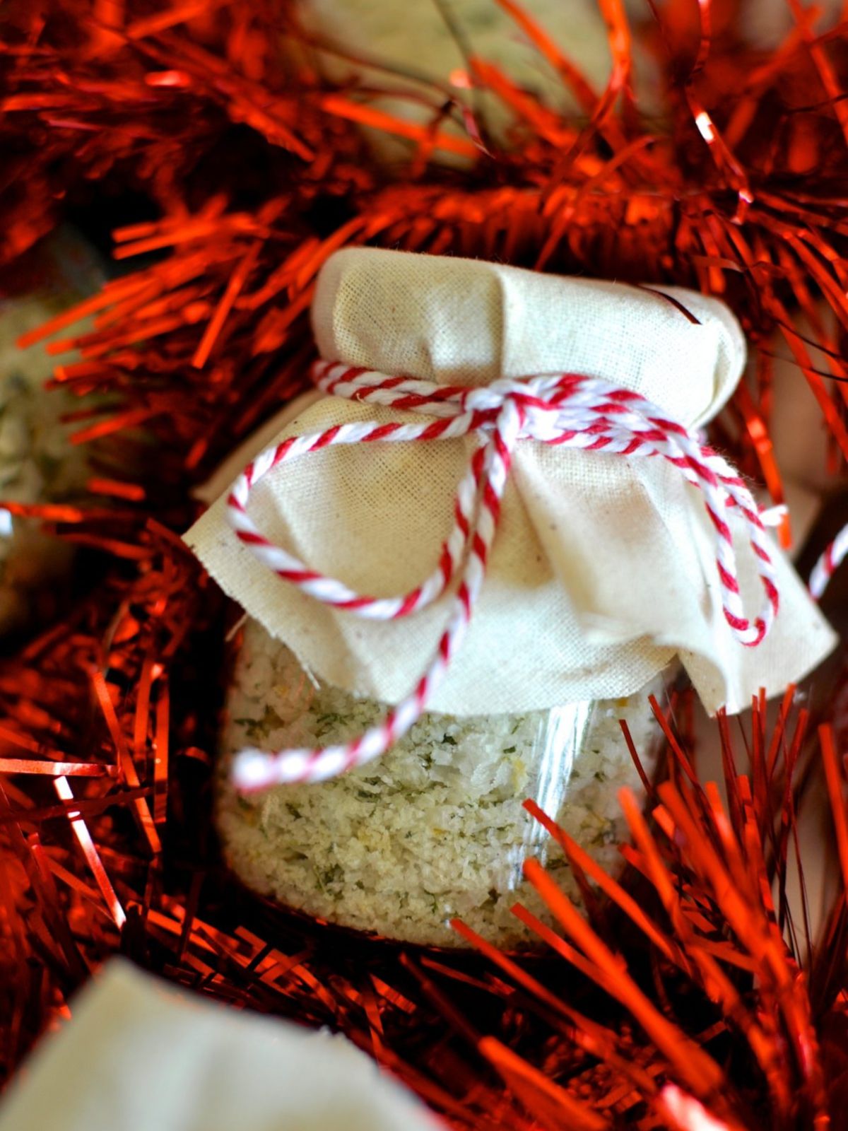 Rosemary and lemon salt in small jar with canvas on top tied with red and white twine on bed of red tinsel.