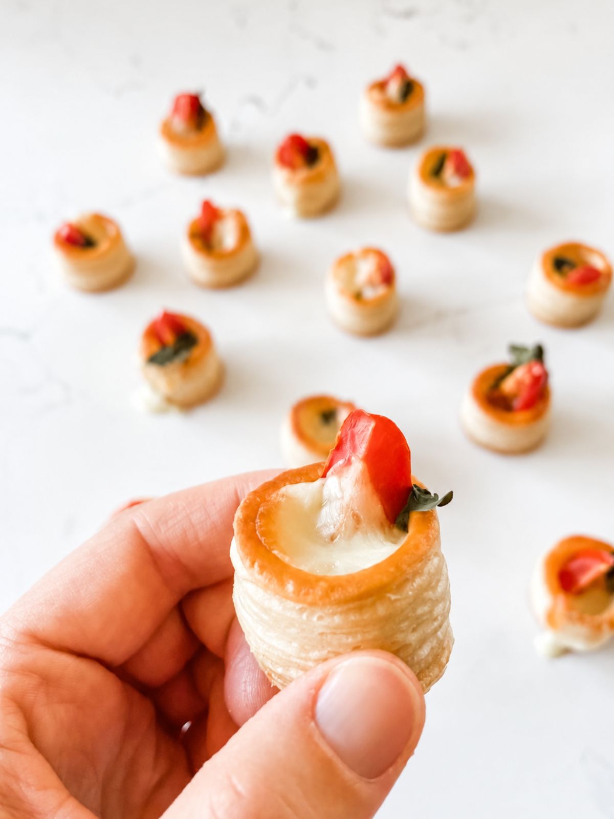 Easy Christmas Vol-au-vent Recipe With Tomato + Cheese held in hand in front of white marble bench.