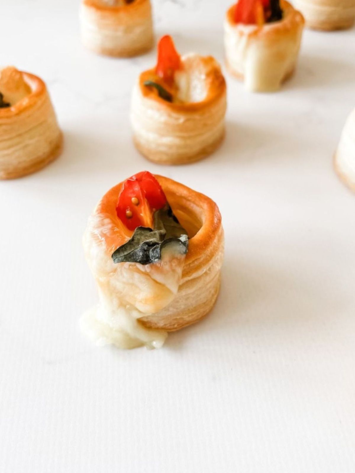 Easy Christmas Vol-au-vent Recipe With Tomato + Cheese oozing cheese on a white marble benchtop.