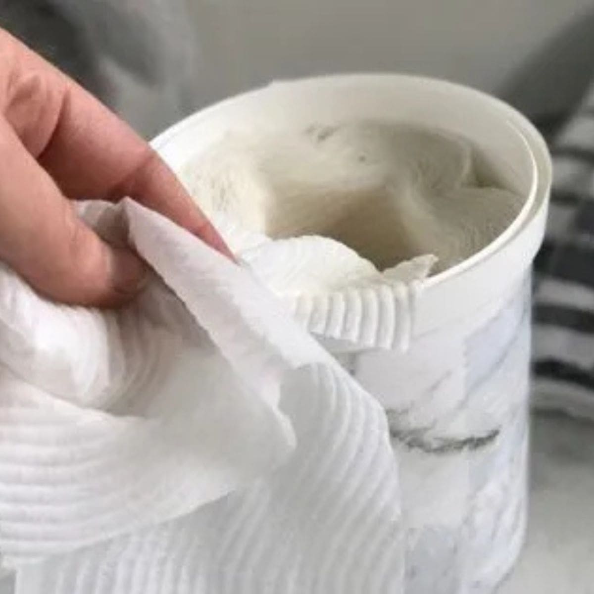 Homemade baby wipes - paper towel in a white tub. Hand pulling one wipe out of the container.
