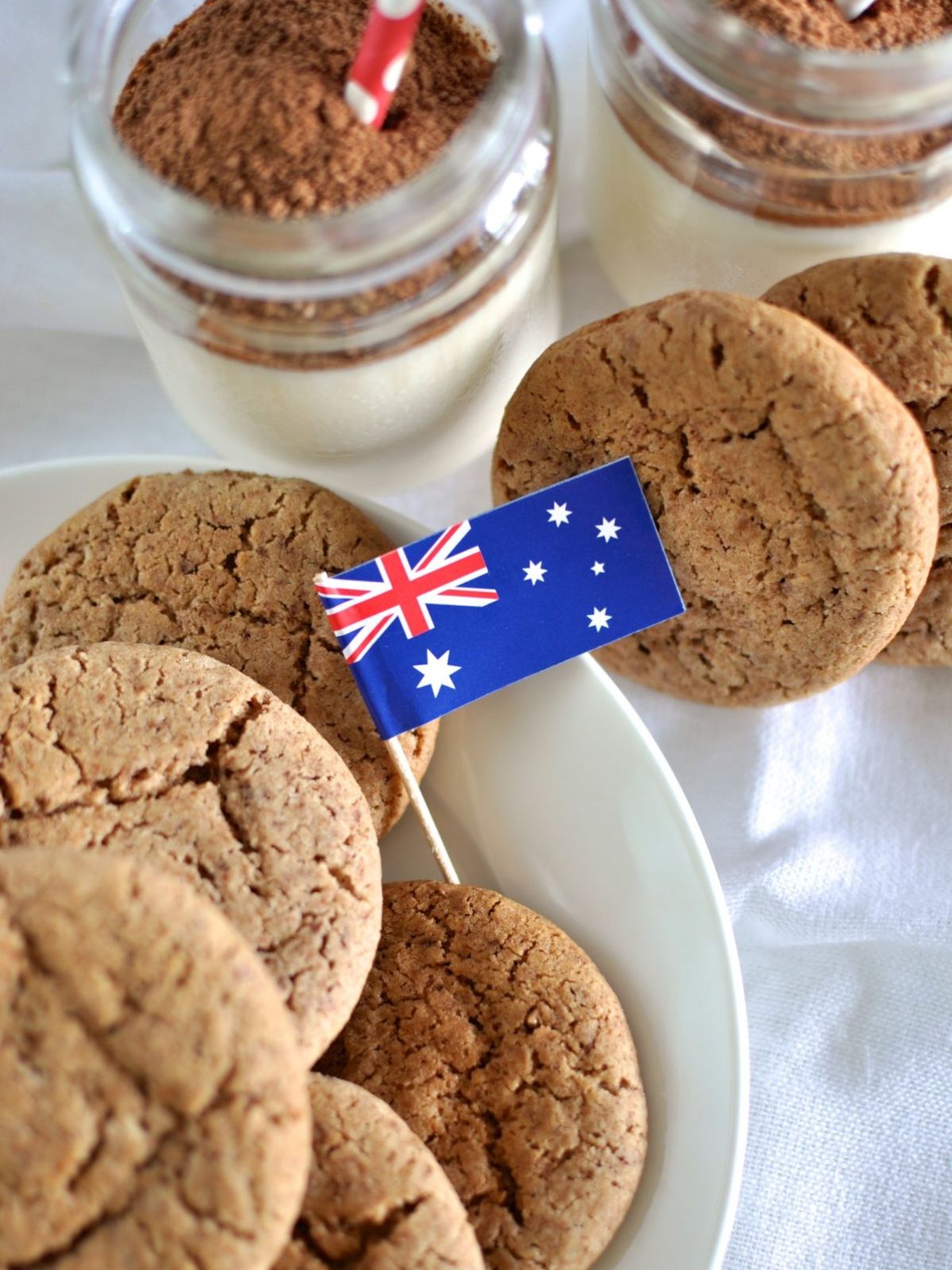 Milo Biscuits on a plate with a small Australian flag & glass of milk and Milo in the background. 