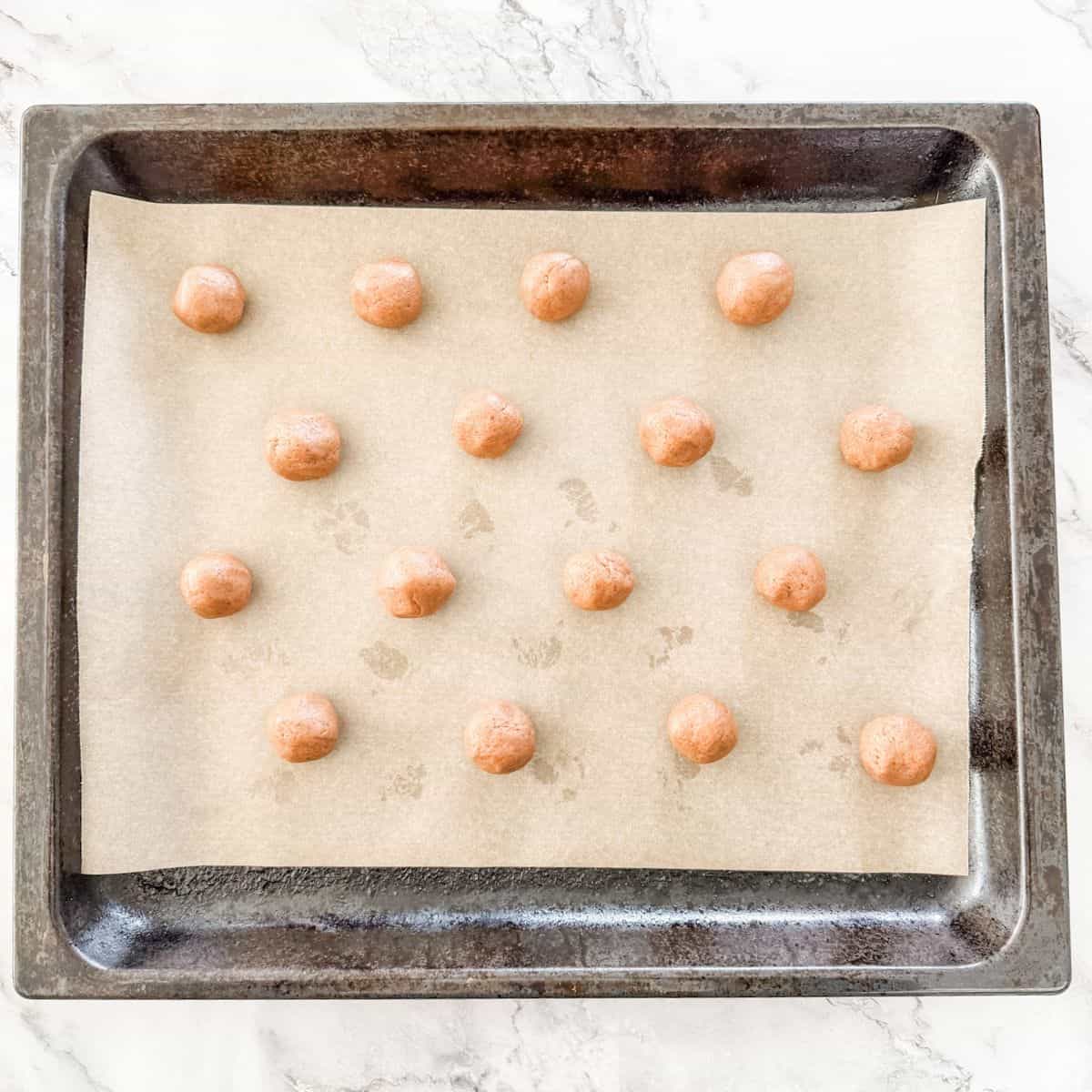 Balls of Milo Biscuit dough on a parchment paper lined oven tray. 
