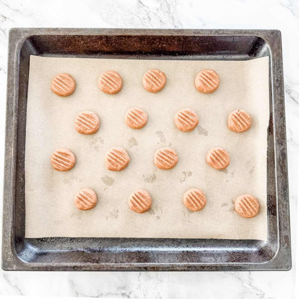 Balls of Milo Biscuit dough on a parchment paper lined oven tray pressed down with fork. 