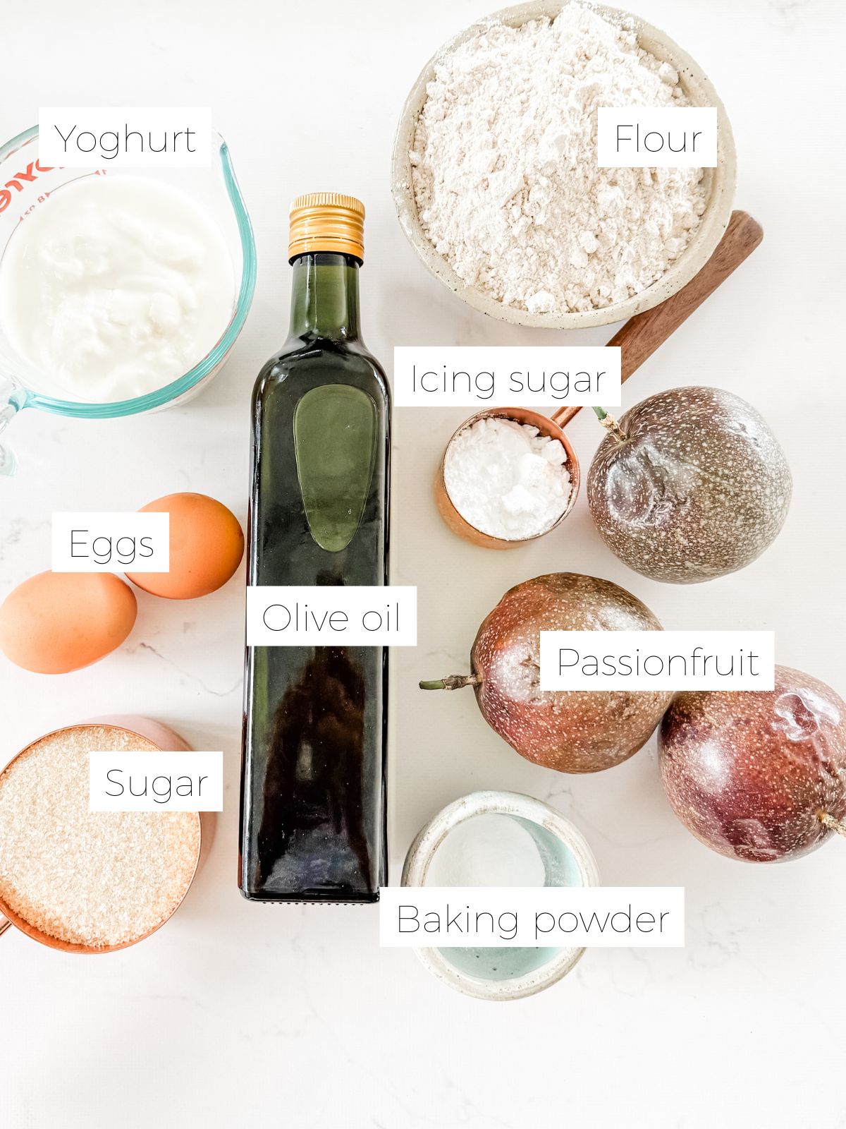 Ingredients in Easy Passionfruit Yoghurt Cake - Bottle of oil, eggs, sugar, passionfruit, bowl of baking powder, flour and youghurt on white marble bench. 