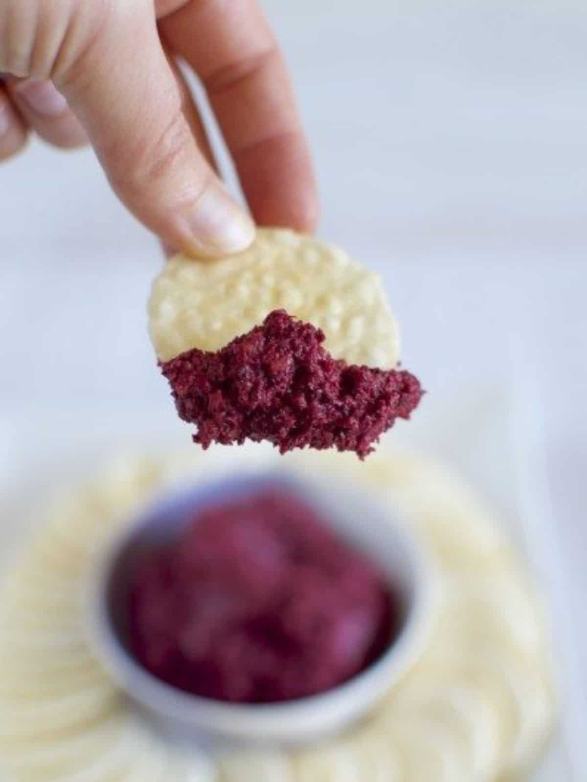 Scooping a serve of beetroot dip from a bowl with a rice cracker. 