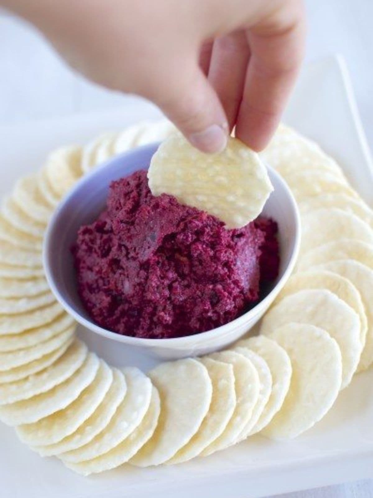 Bowl of beetroot and walnut dip surrounded by rice cracker biscuits. 