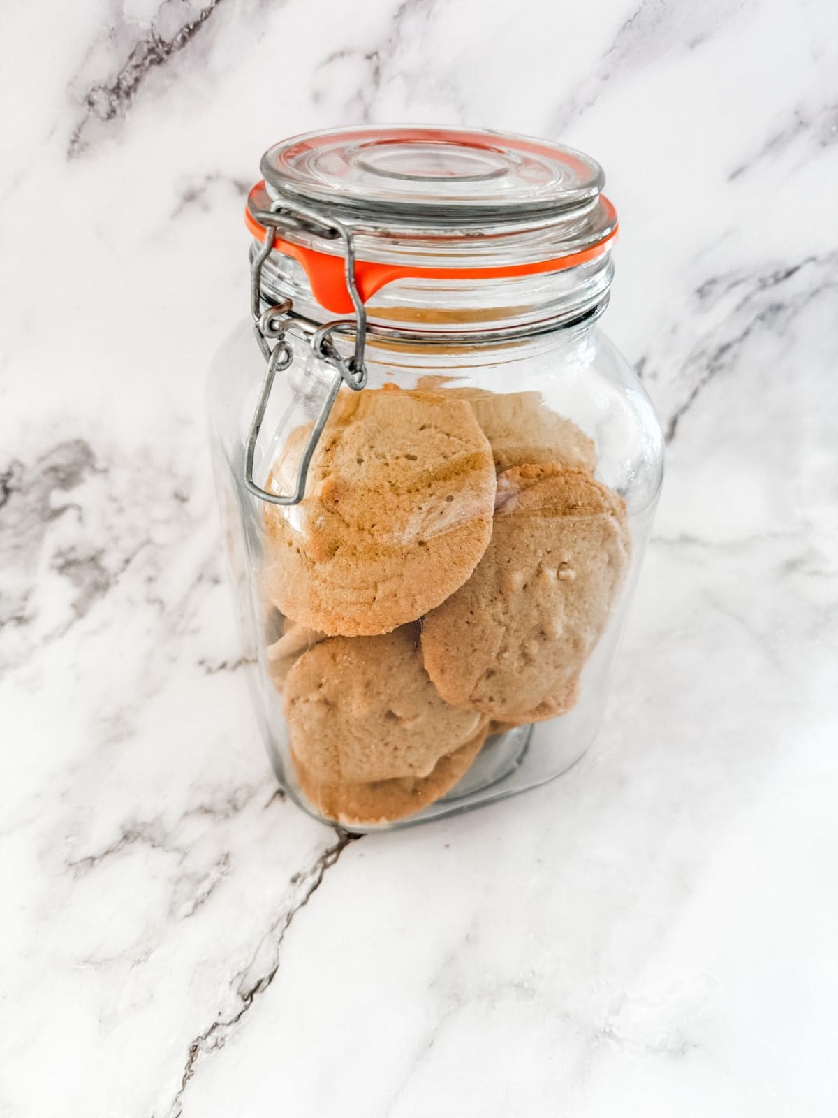 Brown sugar walnut cookies in a glass cookie jar on a white marble bench top.