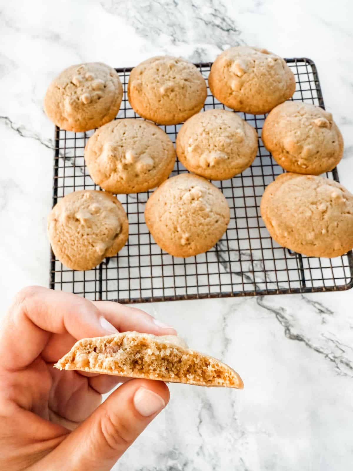 Hand holding half a brown sugar walnut biscuit with a tray of cookies cooling in the background.