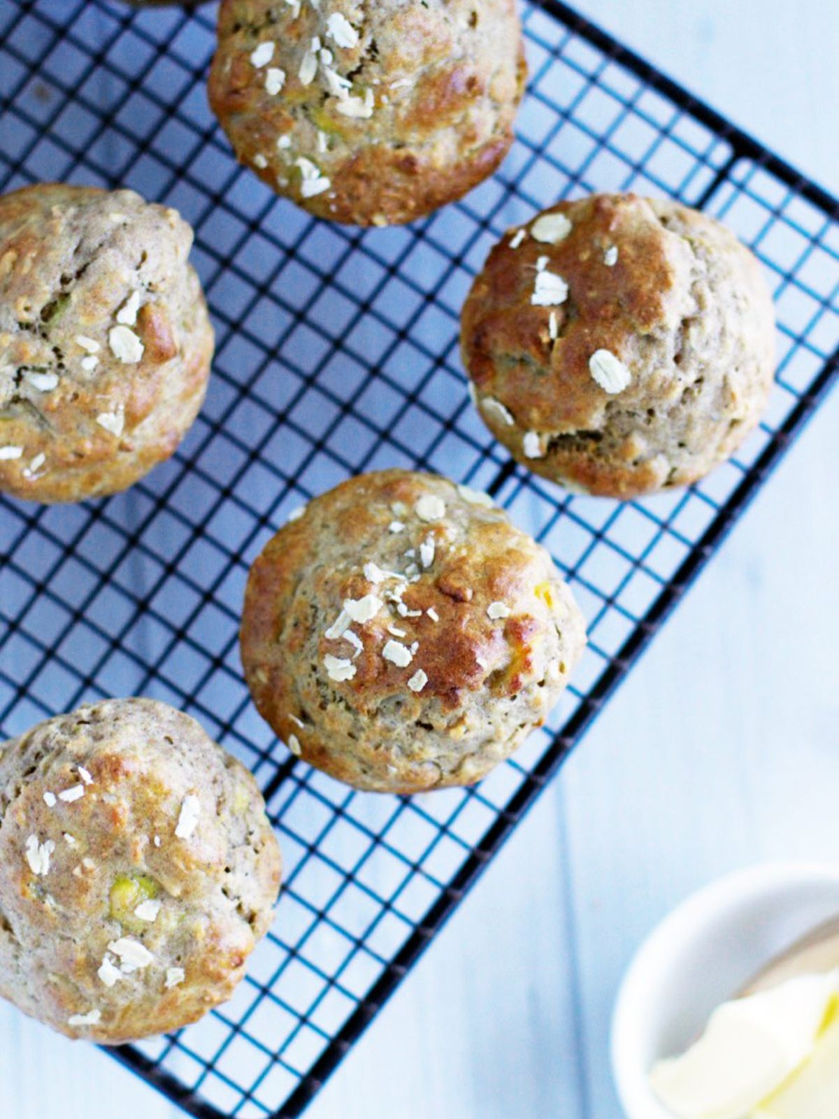 Banana muffins topped with oats sitting on black wire rack cooling.