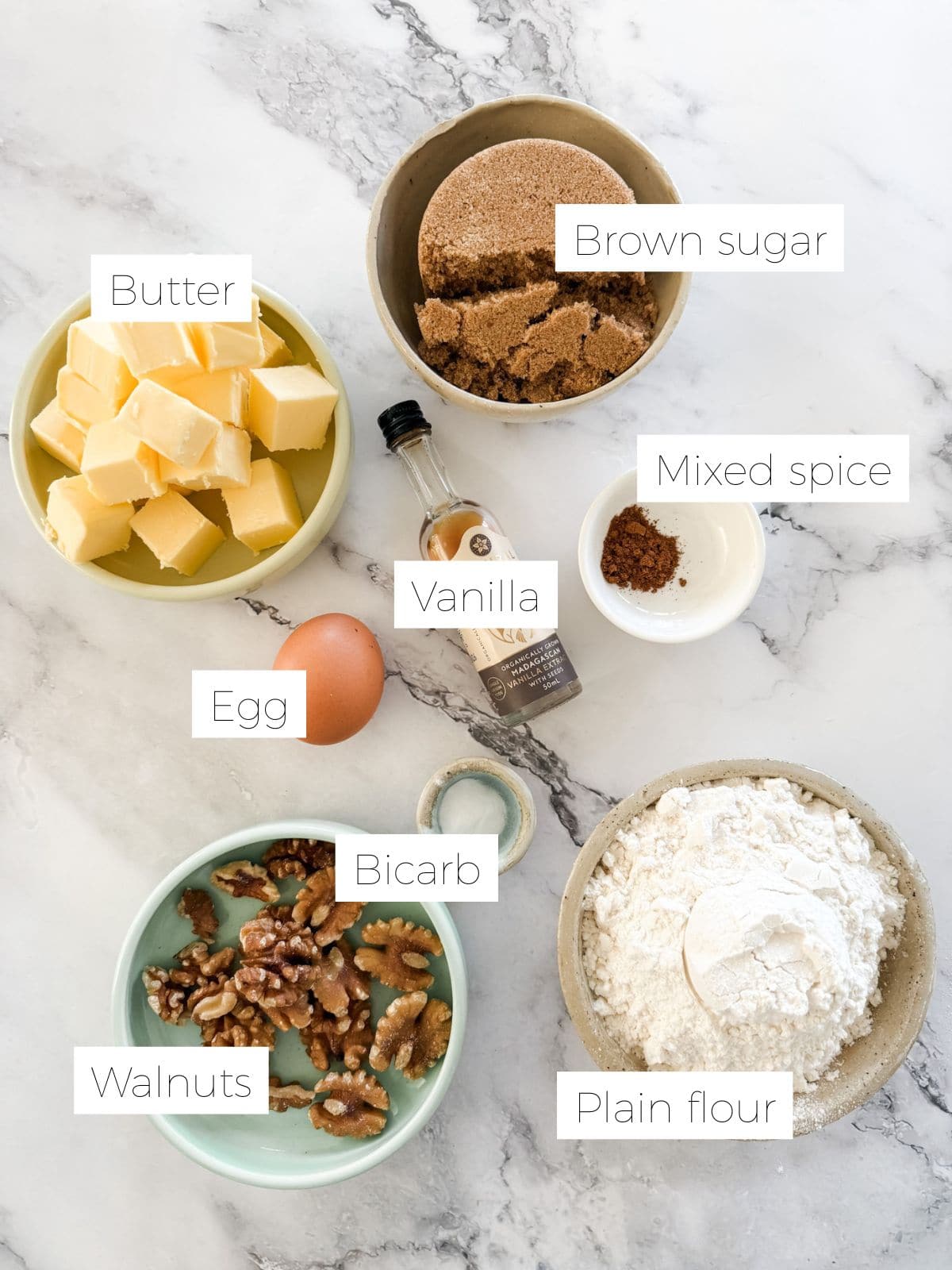 Ingredients for brown sugar walnut biscuits. Bowl of butter, brown sugar, mixed spice, bicarb, flour, walnuts and an egg & bottle of vanilla.