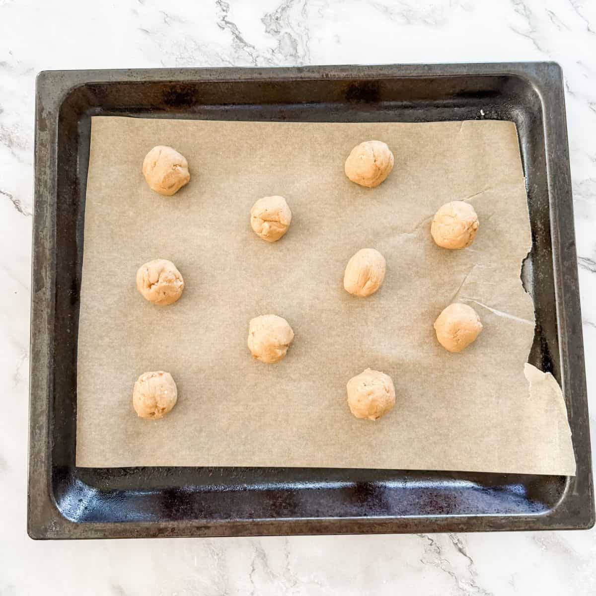 Balls of light brown cookie dough on a baking paper lined oven tray