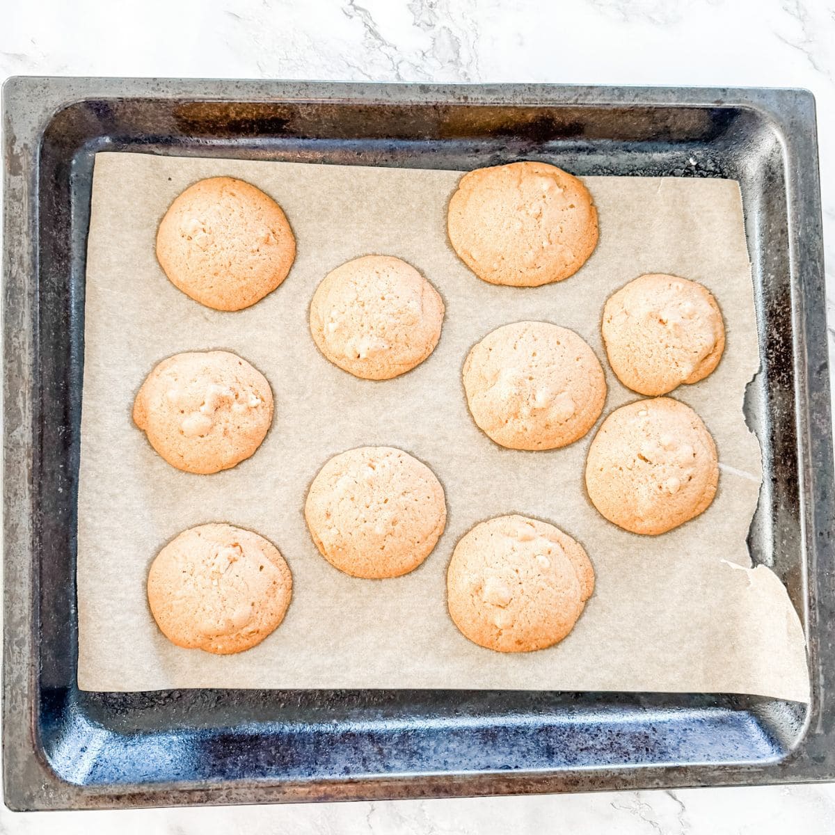 Light brown cookies freshly baked on a brown paper lined oven tray.