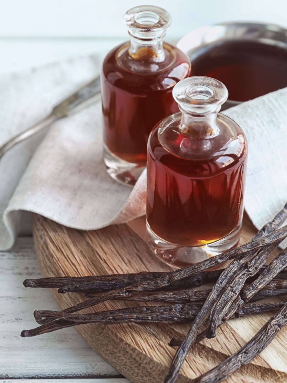 Two small bottles of homemade vanilla extract with vanilla beans on a timber chopping board. 