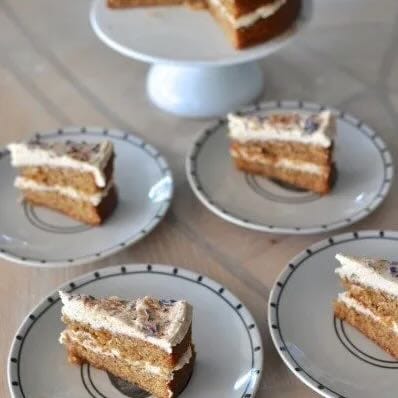 Two layer cinnamon pound cake with white icing in the middle and top sprinkled with lavender flowers. Cut in slices on plates.