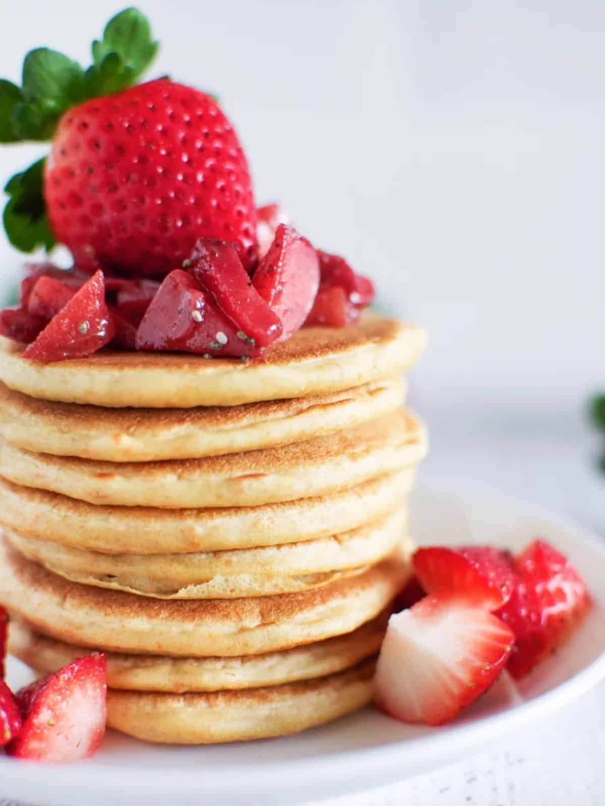 Sourdough pancake stack on a round white plate topped with fresh strawberries