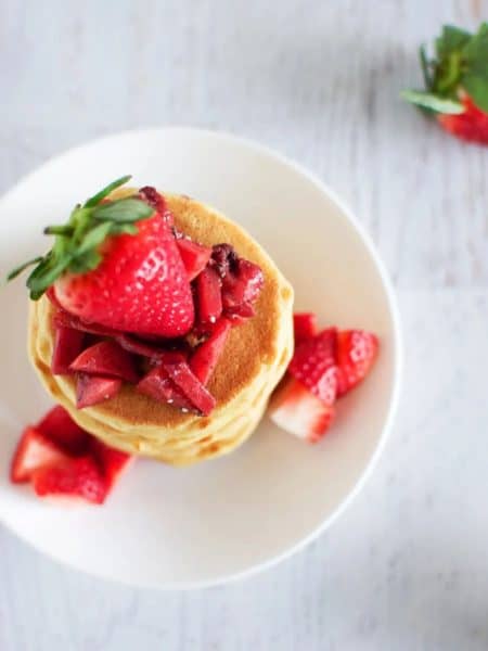 Sourdough pancake stack on a round white plate topped with fresh strawberries