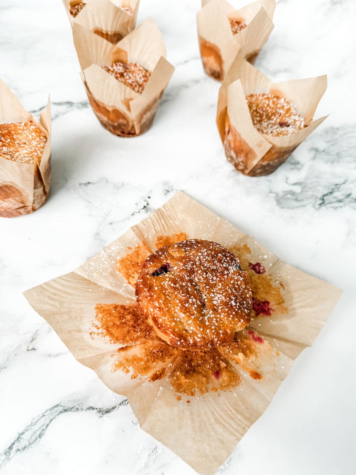 6 raspberry and white chocolate muffins in brown paper wrappers on white marble benchtops