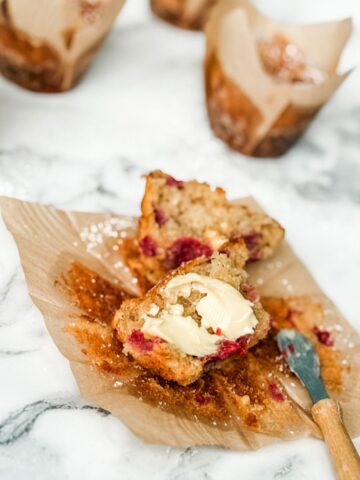 White chocolate and raspberry muffin split in two spread with butter with small butter knife.