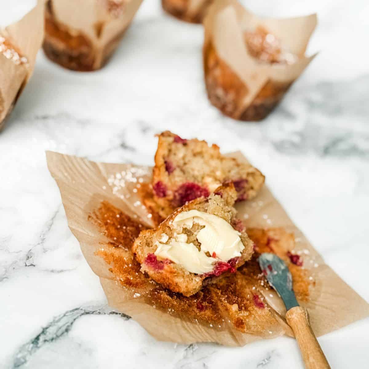 White chocolate and raspberry muffin split in two spread with butter with small butter knife.