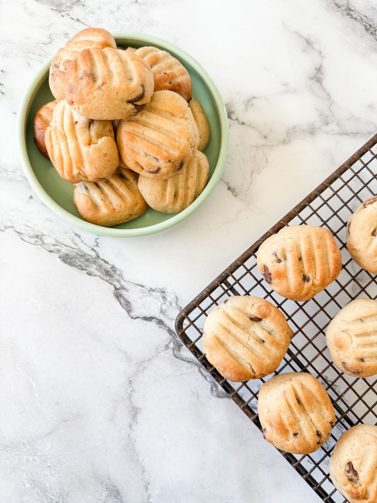 Sante biscuits - chocolate chip cookies in a bowl with some one a cooling rack on a white marble bench top.
