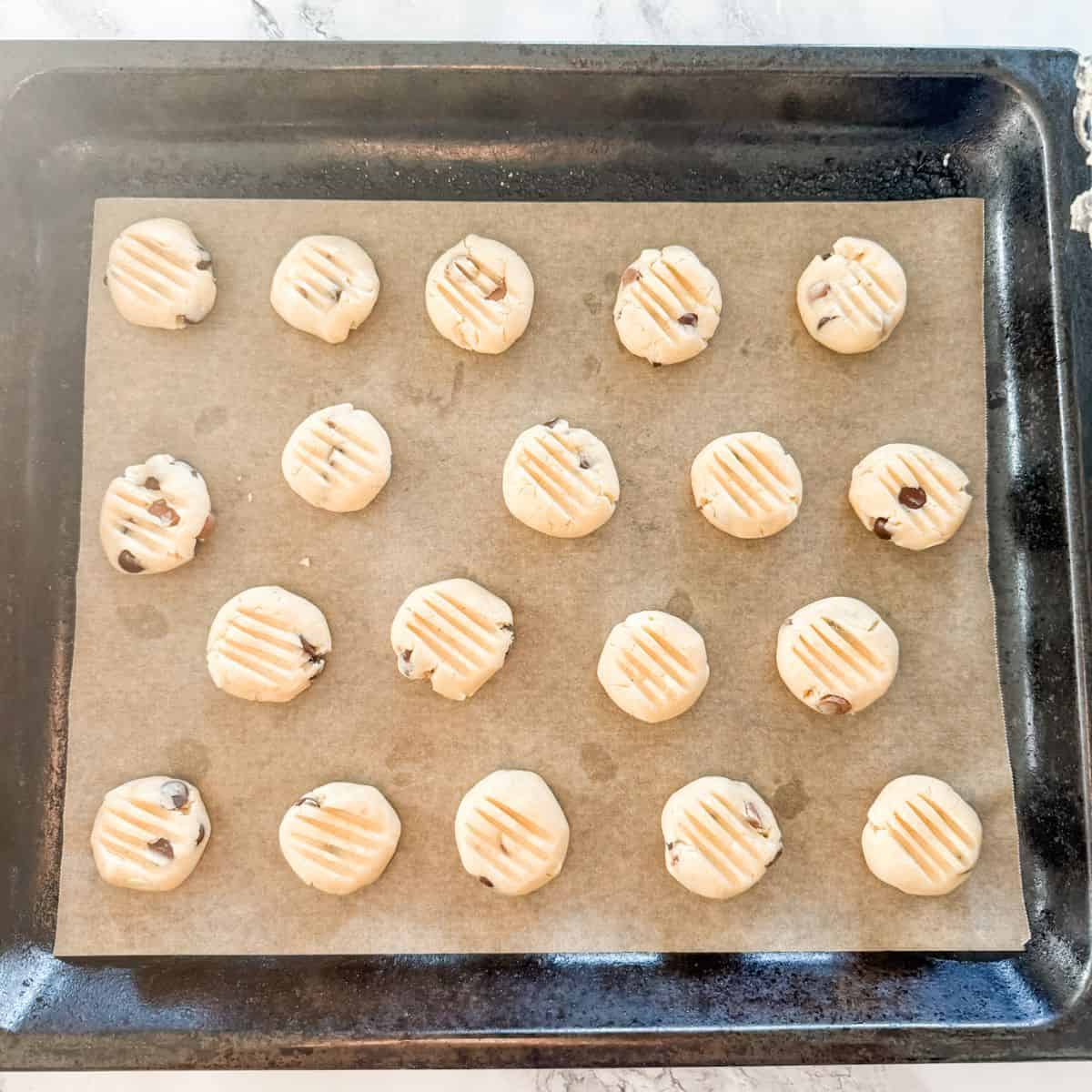 Balls of Sante chocolate chip cookie dough on a lined baking tray pressed with a fork.