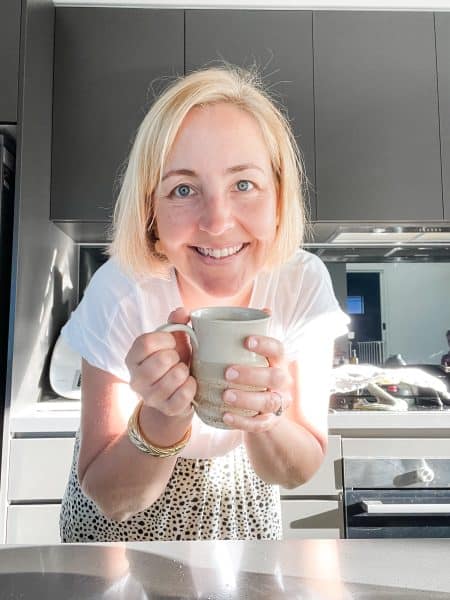 Claire headshot - Claire from Claire K Creations. 38 year old woman with short blonde hair holding a tea cup standing in a kitchen