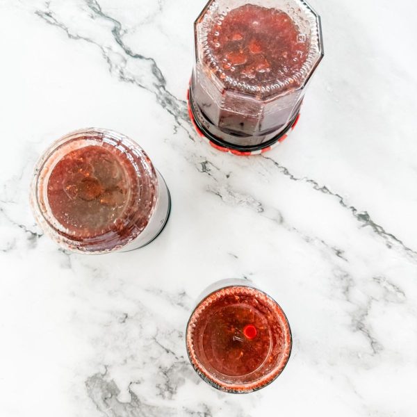 Homemade strawberry jam upside down to seal. 3 jars on a white marble bench.