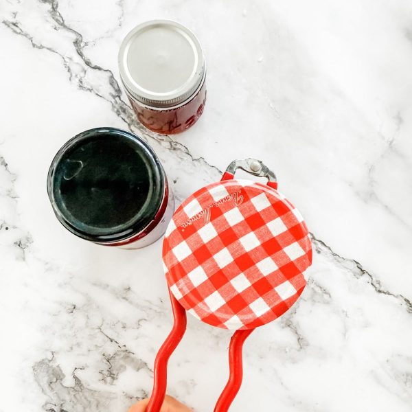 Turning homemade strawberry jam jars onto their heads using a jar holder.