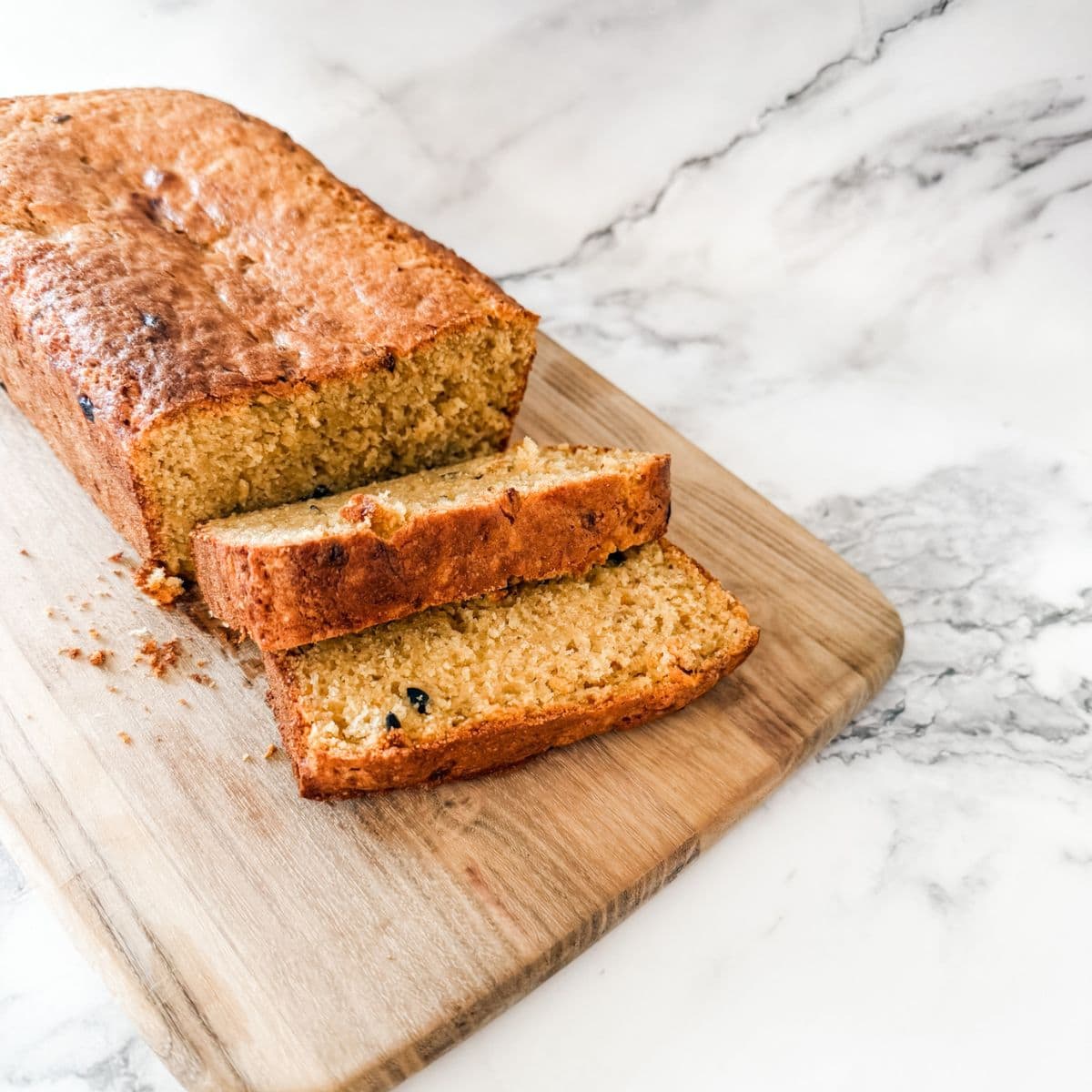 Banana and passion fruit loaf - two slices cut on wooden chopping board on white marble bench.