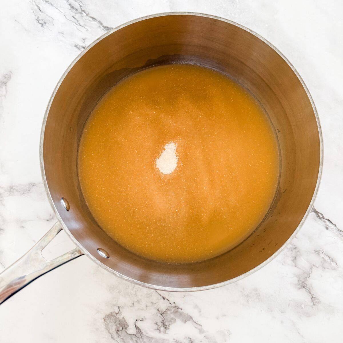 Stainless steel pot with juice, gelatine and honey on a white marble bench top - making jelly lollies. 