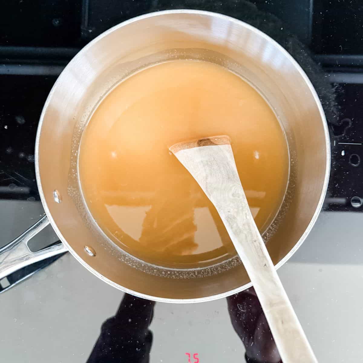 Stainless steel pot with juice, gelatine and honey heating on a black cook top - making jelly lollies.