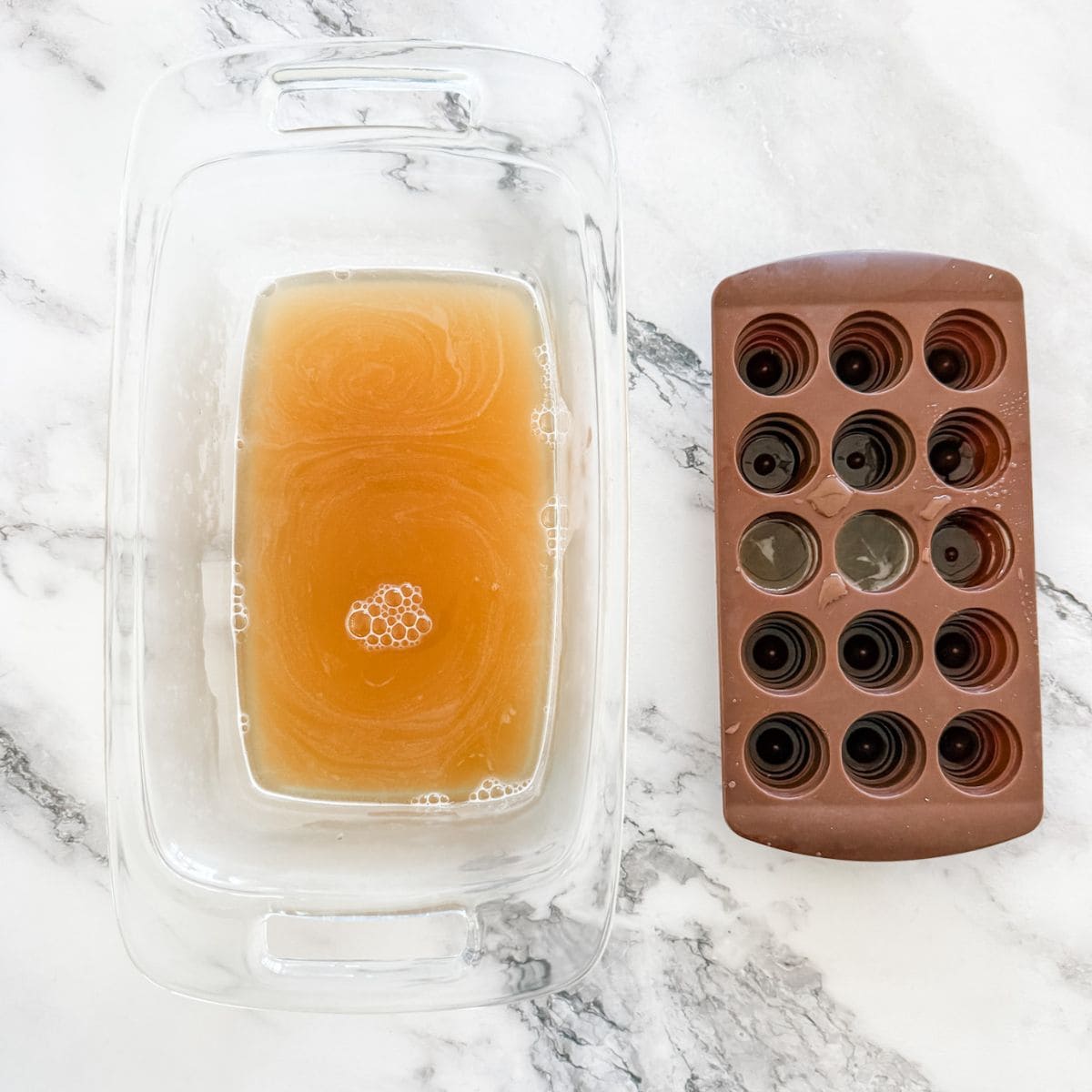 Apple juice jelly in glass loaf tin with some jelly mix in brown chocolate mould on white marble benchtop. 