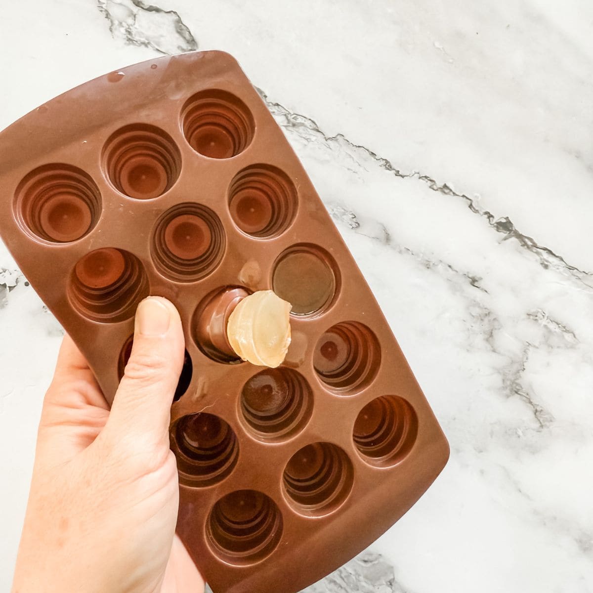 Removing jelly from a brown chocolate mould on a white marble bench top. 