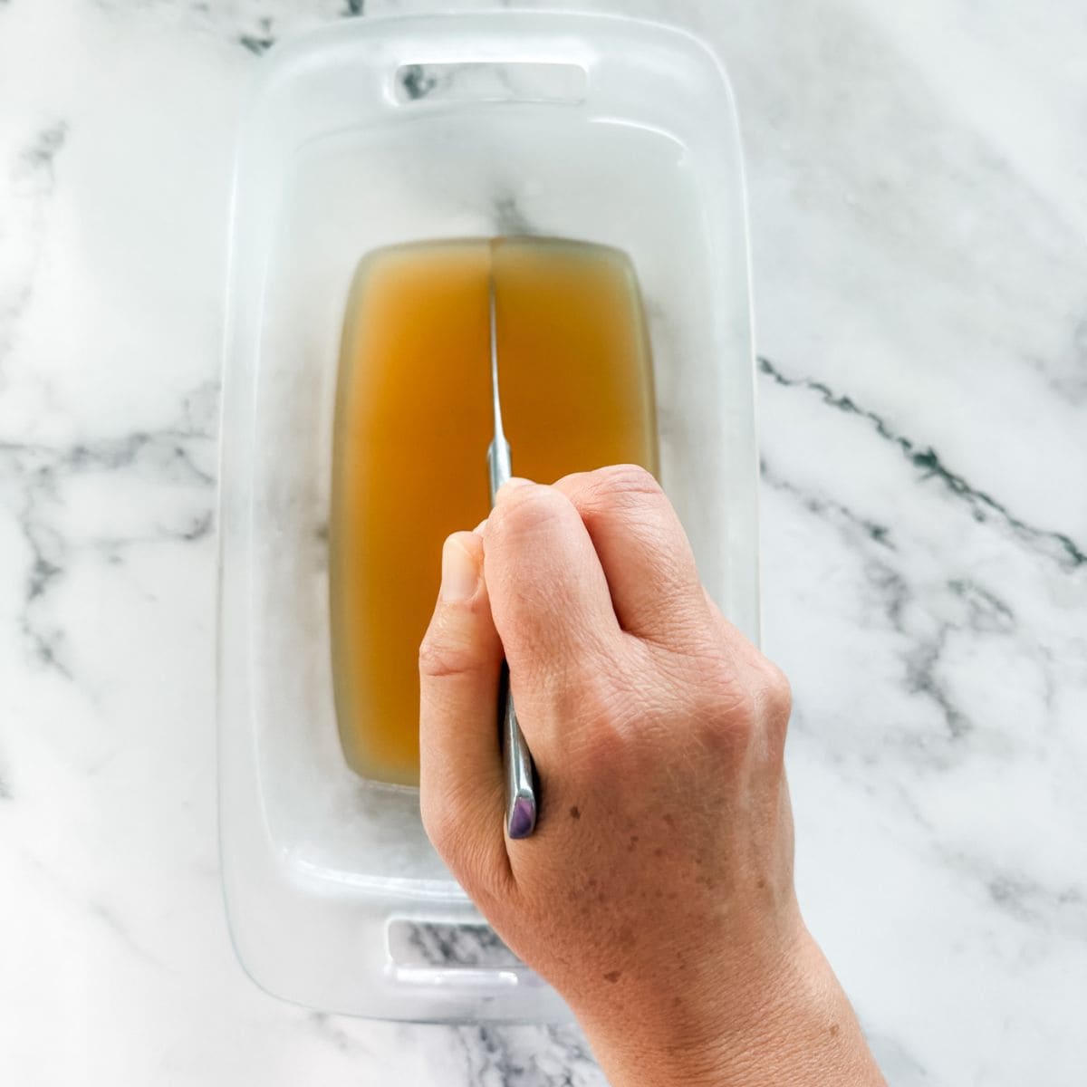 Cutting jelly in glass loaf tin making jelly lollies on a white marble bench top.